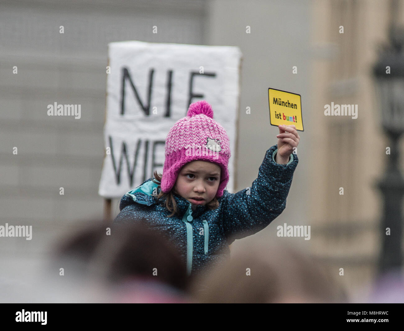 Munich, Bavaria, Germany. 17th Mar, 2018. A child holds a ''Muenchen ist Bunt'' card, which roughly translates to ''Munich is diverse''. Protesting against the arrival of Pegida Dresden's Lutz Bachmann and Sigfried Daebritz in Munich, no less than three demonstrations were organized by the city, including a Muenchen ist Bunt and Bellevue di Monaco protest at Max Joseph Platz. At this demonstration, choirs were in attendance, along with celebrities, politicians, and other prominent Muenchners dressed as doctors in order to tell Pegida that they will help them go back to Dresden. Participa Stock Photo