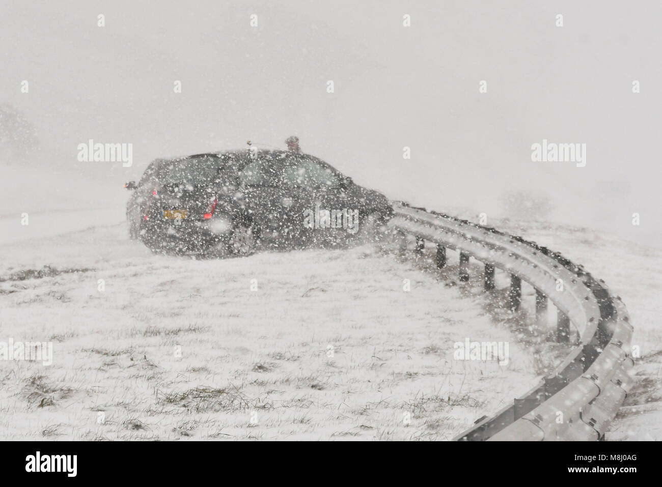 Long Bredy, Dorset, UK.  18th March 2018.  UK Weather.  (Sequence of Images of an accident  5 of 5) A car swerves on the road and hits the crash barriers in the central reservation as the driver is unable to stop to avoid stationary cars which have stopped in Blizzard Conditions on the A35 at Long Bredy between Bridport and Dorchester in Dorset as heavy snow which has covered the road, makes driving hazardous.  Picture Credit: Graham Hunt/Alamy Live News. Stock Photo