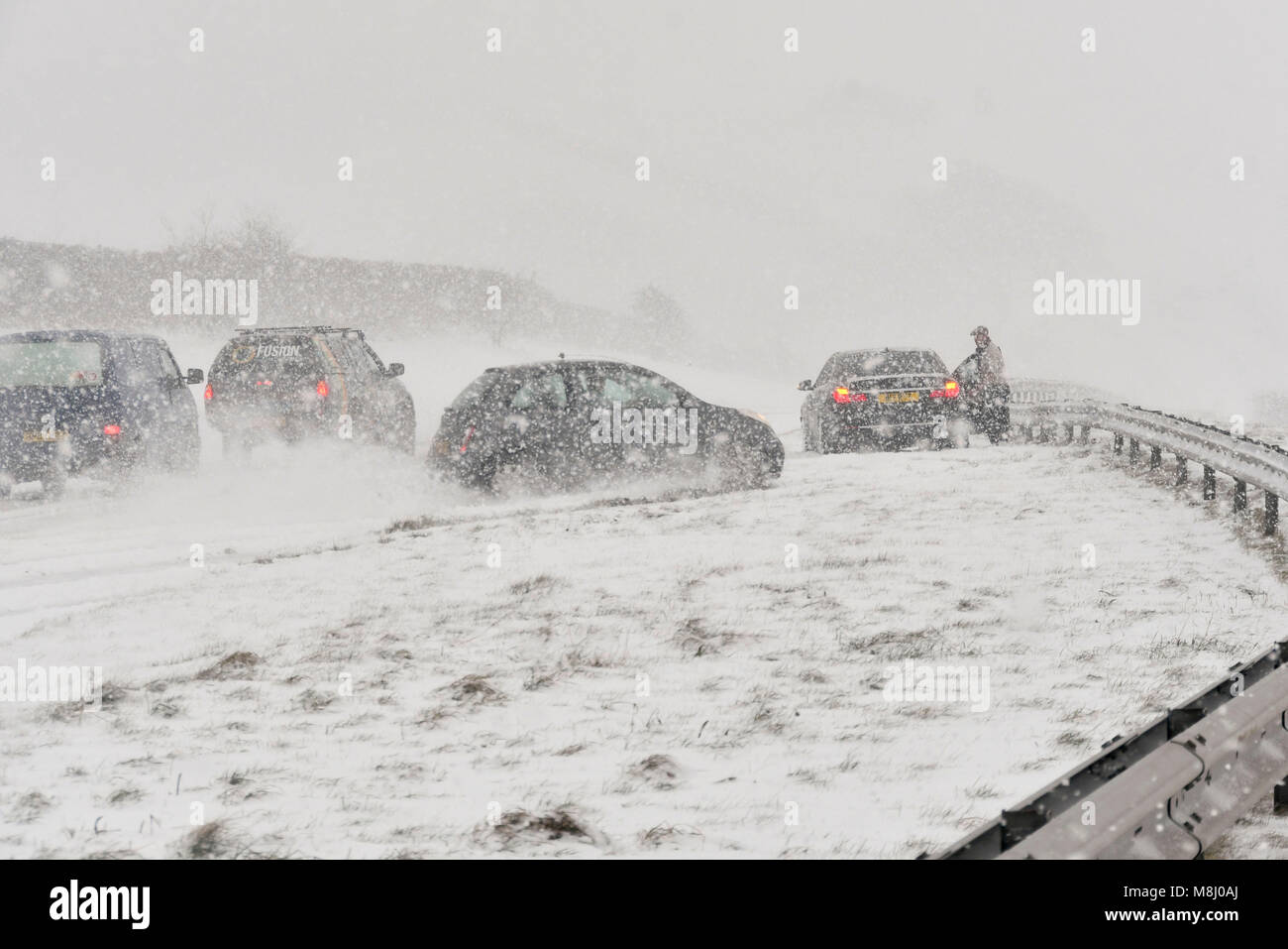 Long Bredy, Dorset, UK.  18th March 2018.  UK Weather.  (Sequence of Images of an accident  4 of 5) A car swerves on the road and hits the crash barriers in the central reservation as the driver is unable to stop to avoid stationary cars which have stopped in Blizzard Conditions on the A35 at Long Bredy between Bridport and Dorchester in Dorset as heavy snow which has covered the road, makes driving hazardous.  Picture Credit: Graham Hunt/Alamy Live News. Stock Photo