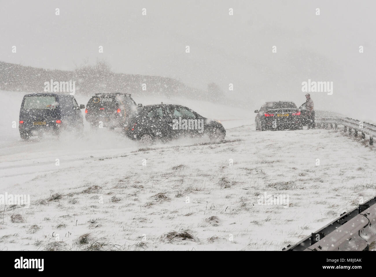 Long Bredy, Dorset, UK.  18th March 2018.  UK Weather.  (Sequence of Images of an accident  3 of 5) A car swerves on the road and hits the crash barriers in the central reservation as the driver is unable to stop to avoid stationary cars which have stopped in Blizzard Conditions on the A35 at Long Bredy between Bridport and Dorchester in Dorset as heavy snow which has covered the road, makes driving hazardous.  Picture Credit: Graham Hunt/Alamy Live News. Stock Photo