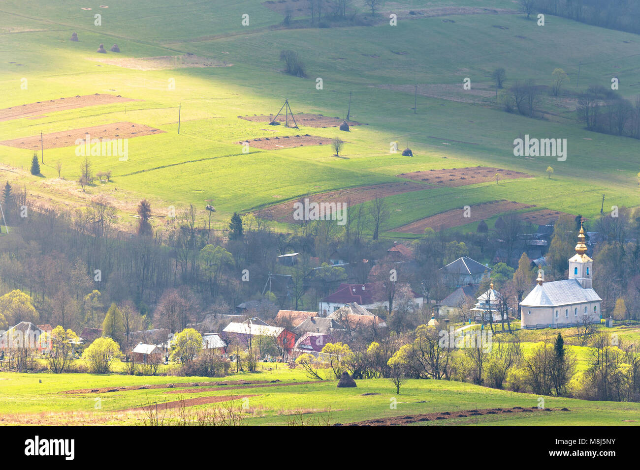 Sunny spring day. Church and village in green mountain valley ...