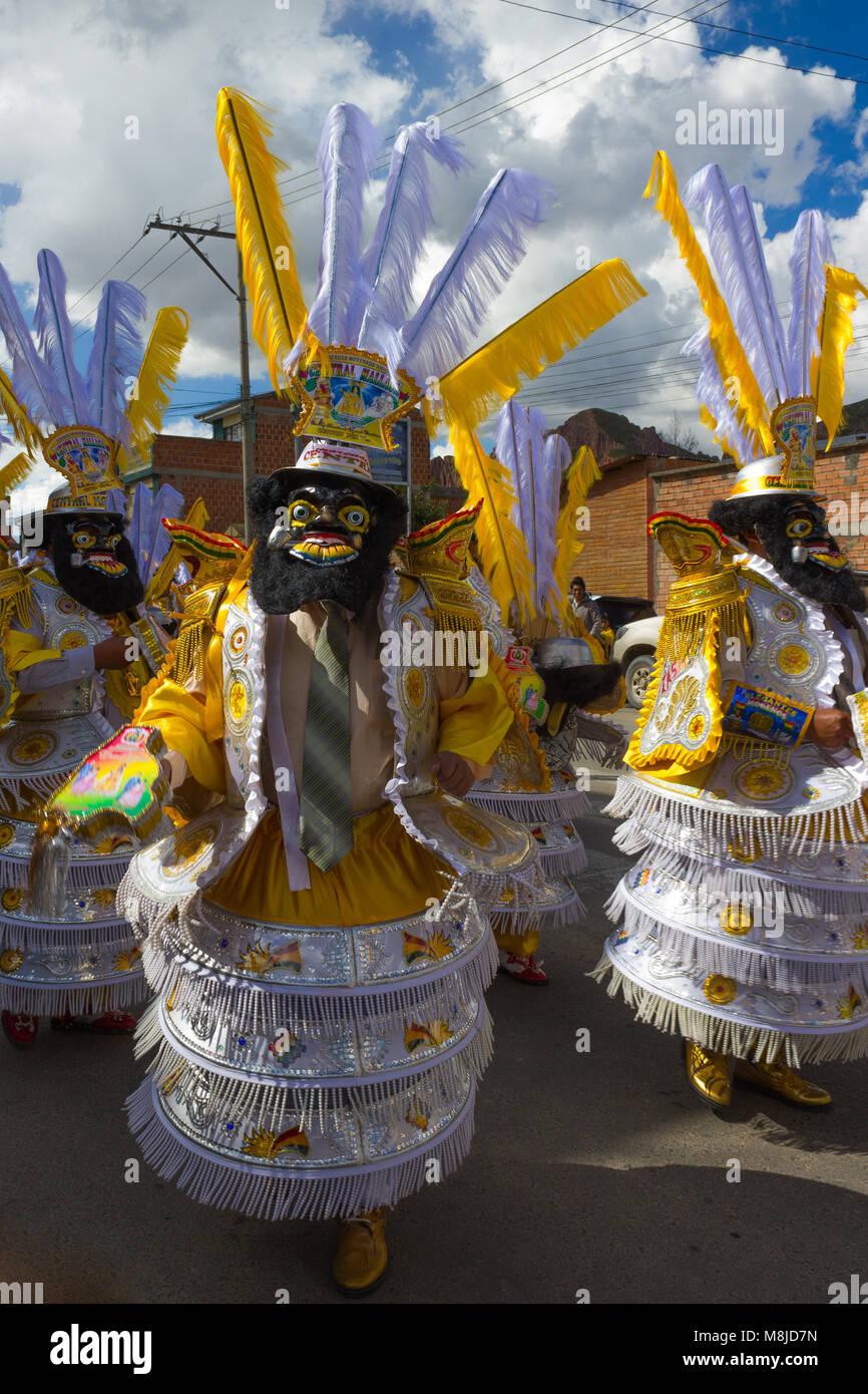 Men in traditional costumes, masks and headdresses in yellow and white in festival parade Stock Photo
