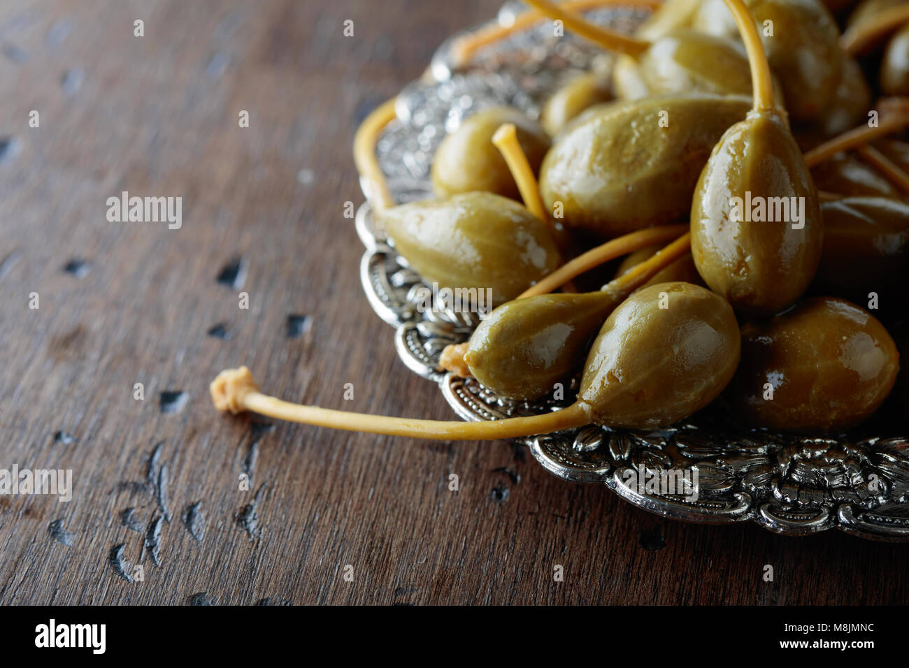 Pickled caper berries in metal dish . Edible fruits of Capparis