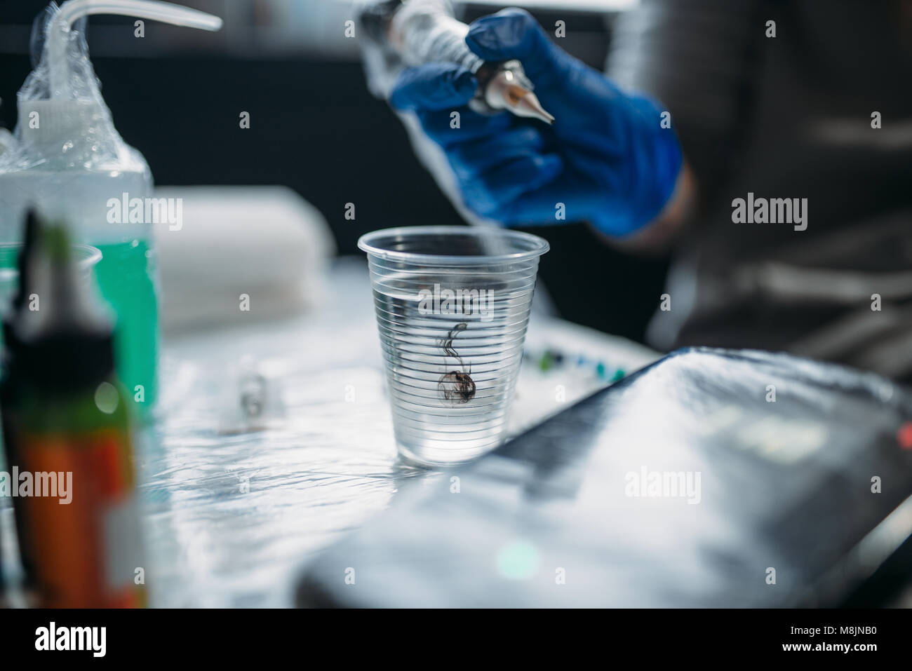 Female tattooist hands in blue sterile gloves holds tattoo machine