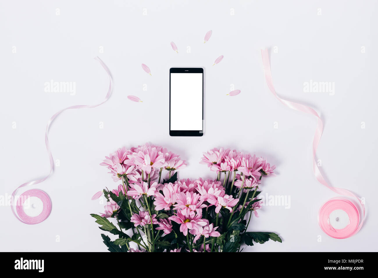 Bouquet of pink flowers, mobile phone with blank screen and ribbons on white table top view