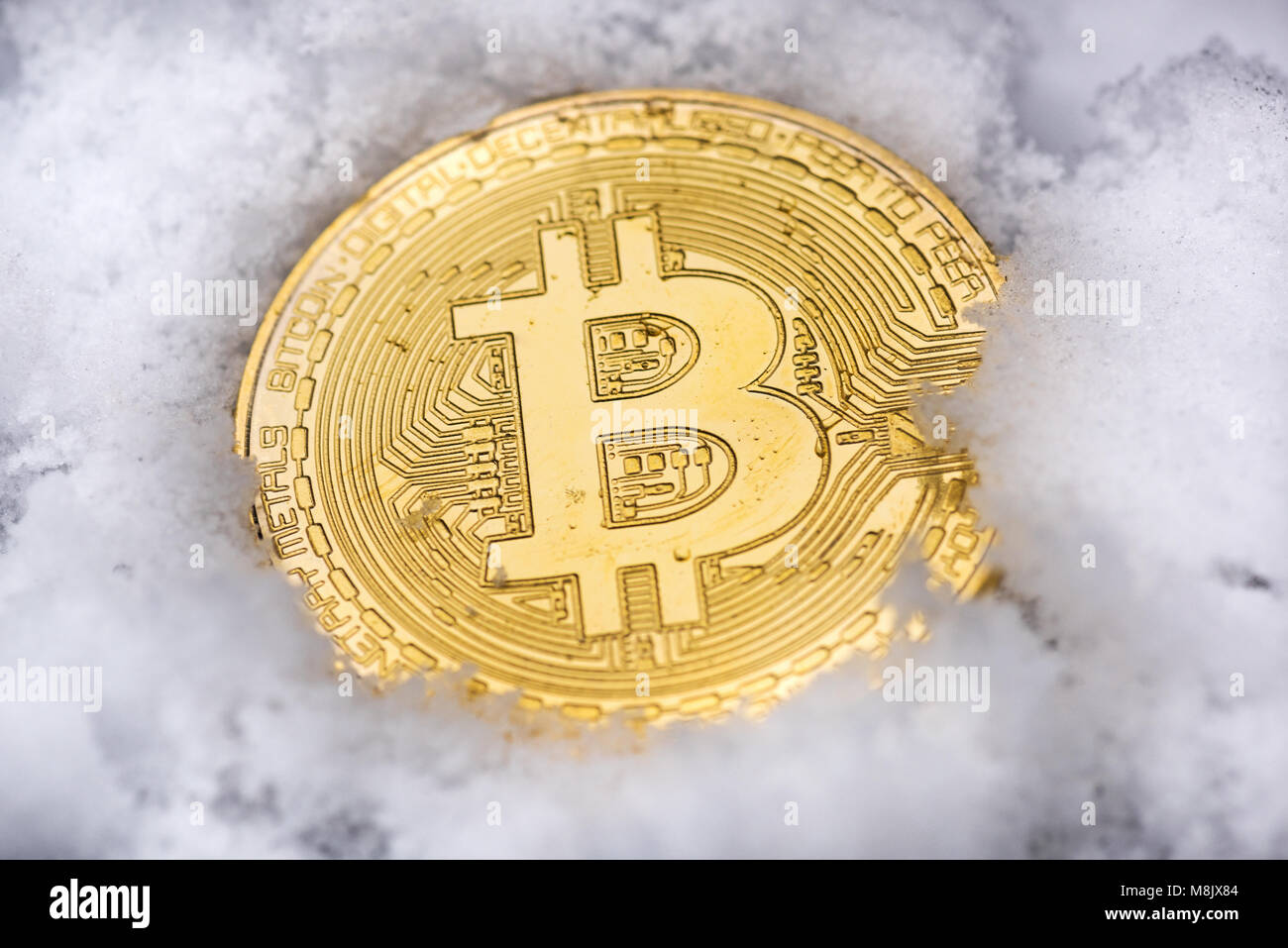 A gold Bitcoin rests in the snow. Stock Photo