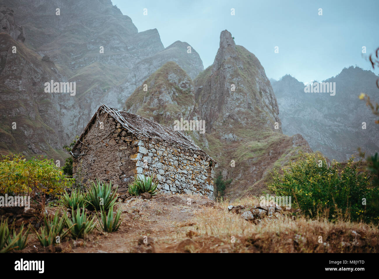 Ruined local storehouse nestled into incredible scenery with steep mountain rocks and vertical peaks. Trekkingtrail on Santo Antao Cape Verde Stock Photo