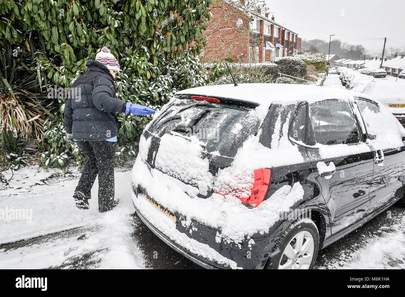 A woman cleans snow off a car in Bristol, where snow fell overnight as the wintry snap dubbed the 'mini beast from the east' keeps its grip on the UK. Stock Photo