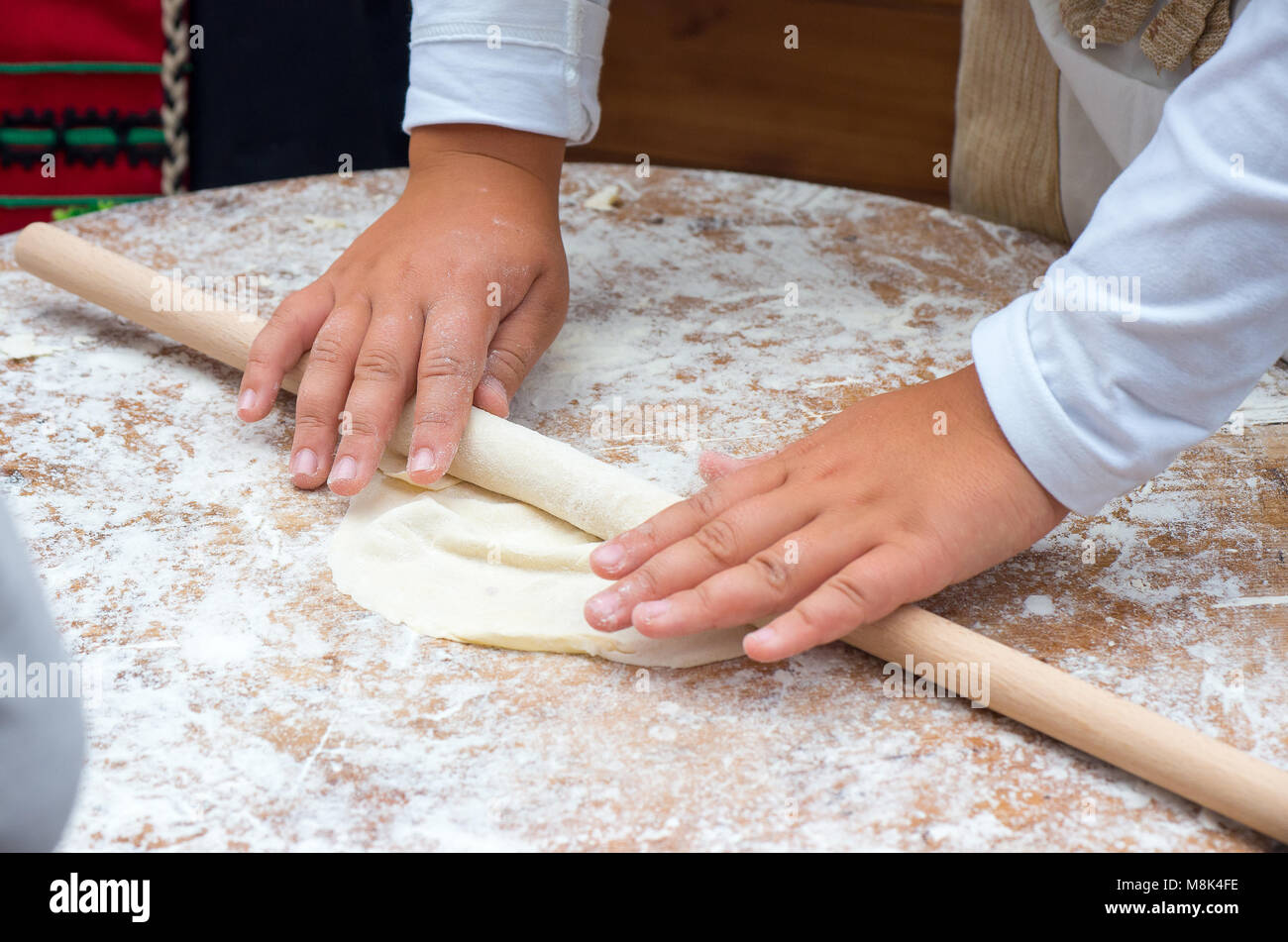 Child hands rolling dough with rolling pin on wooden table Stock Photo