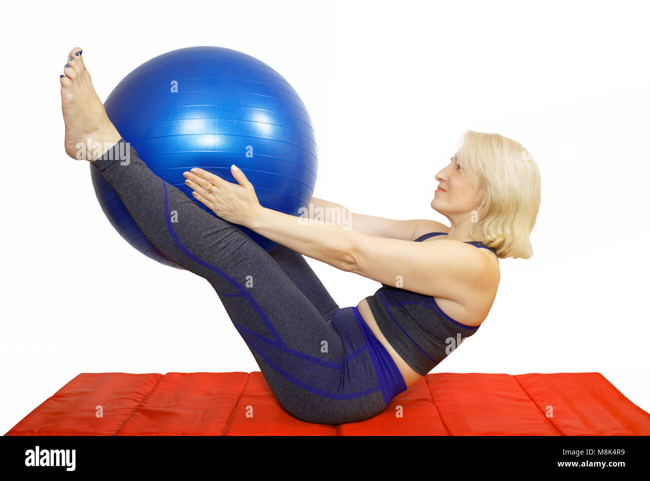 A middle-aged woman performs a physical exercise from Pilates,compresses kicking the ball the fitball and raises them . Exercise for elasticity and bo Stock Photo