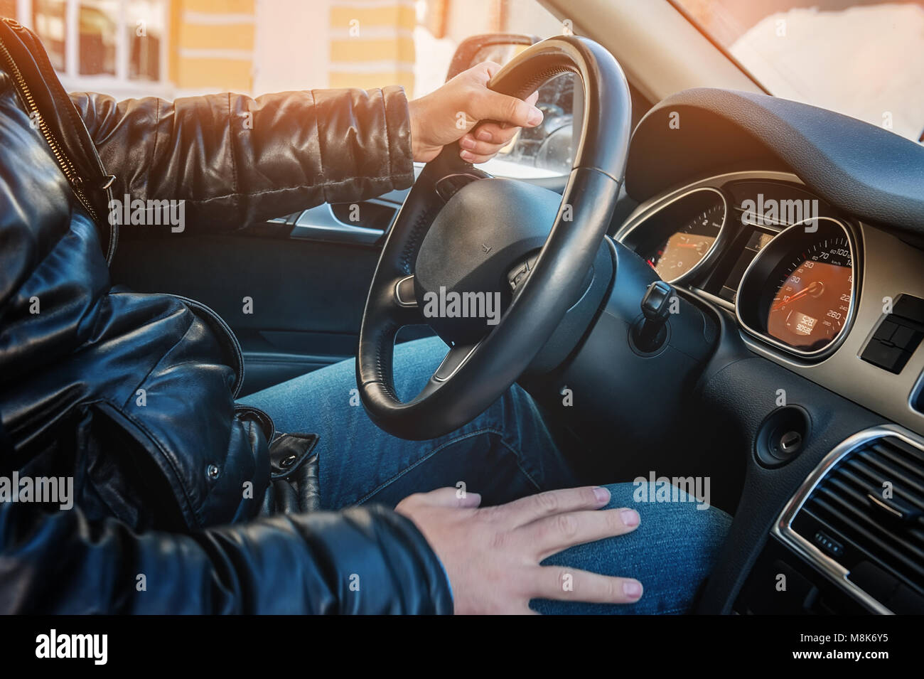 A large man in a leather jacket and jeans sits behind the wheel of a car. Stock Photo