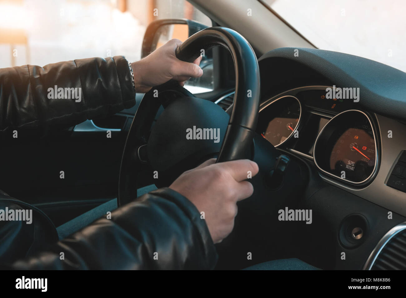 A large man in a leather jacket and jeans sits behind the wheel of a car. Stock Photo