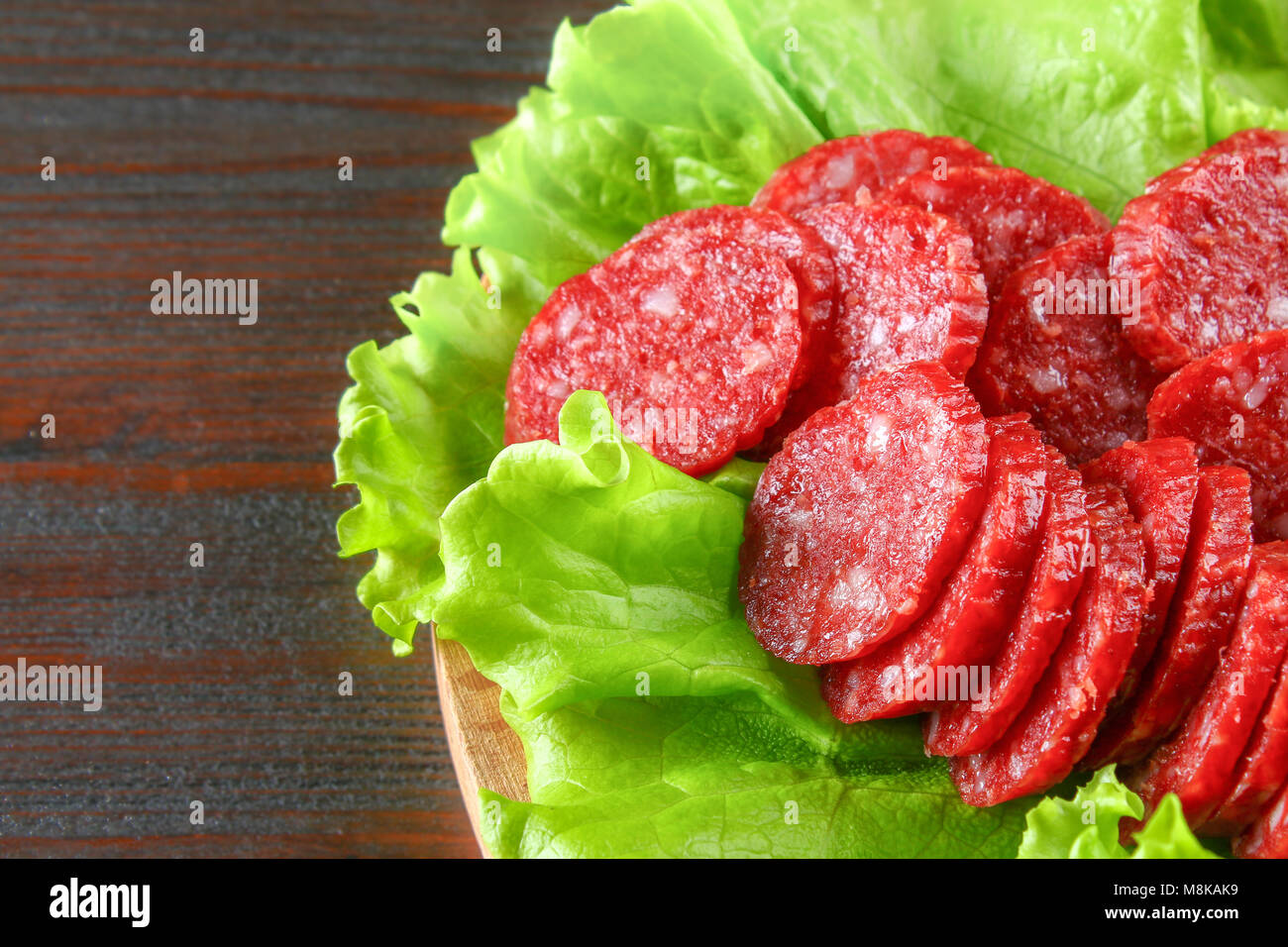 Smoked sausage, salami chopped in slices on a salad on a wooden circular cutting board on a brown table Stock Photo