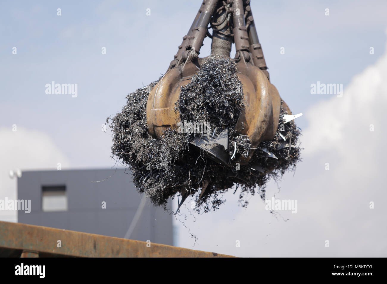 A worker uses a claw excavator to load shredded metal from cars at a