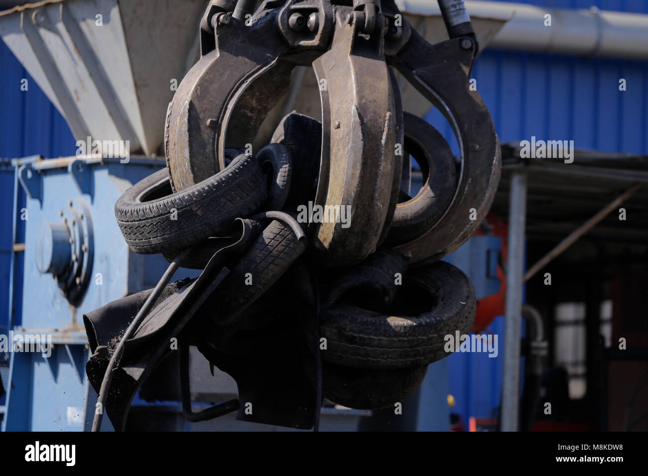 A worker uses a claw excavator to put used car tires in a shredder at a