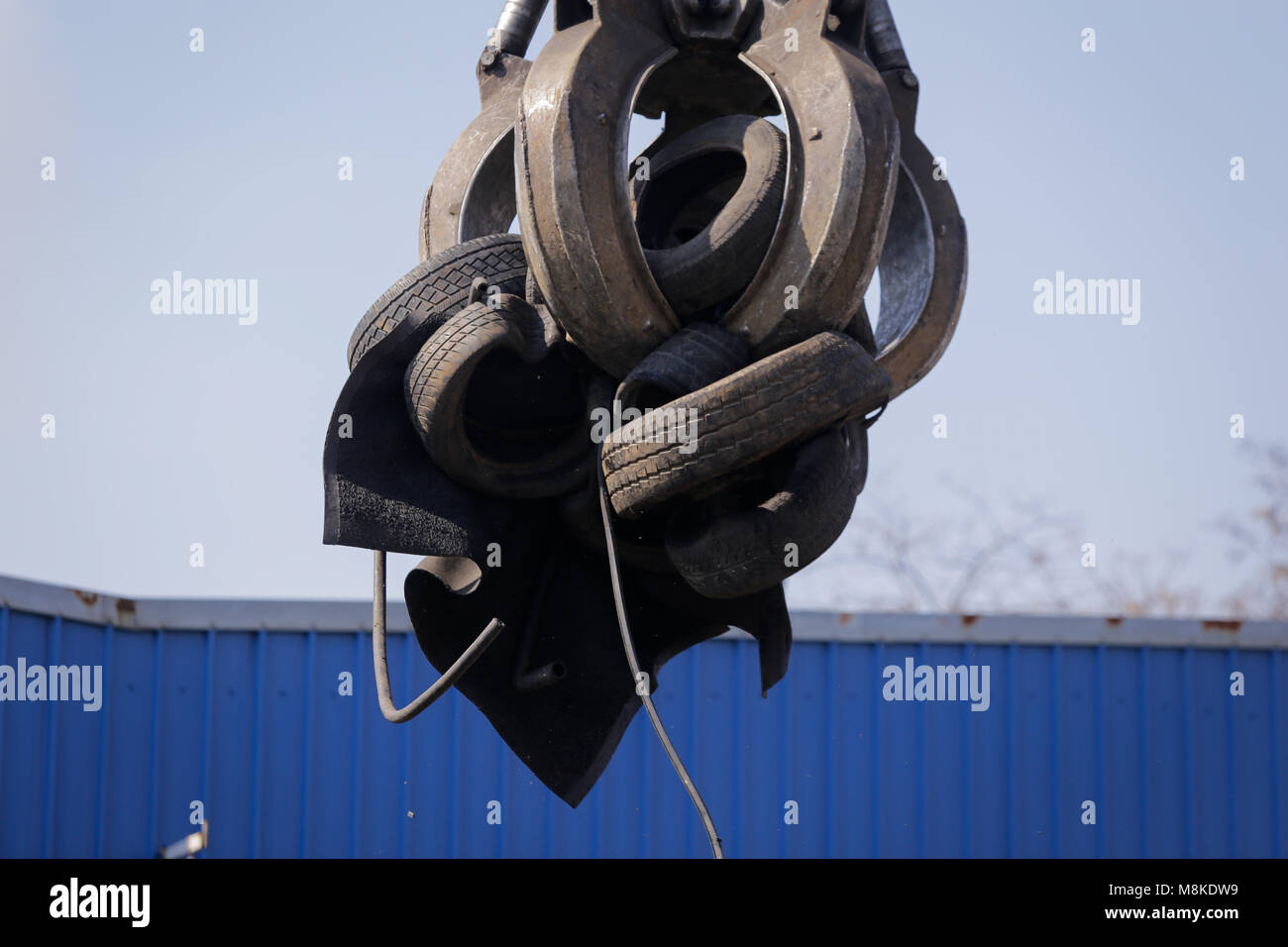 A worker uses a claw excavator to put used car tires in a shredder at a