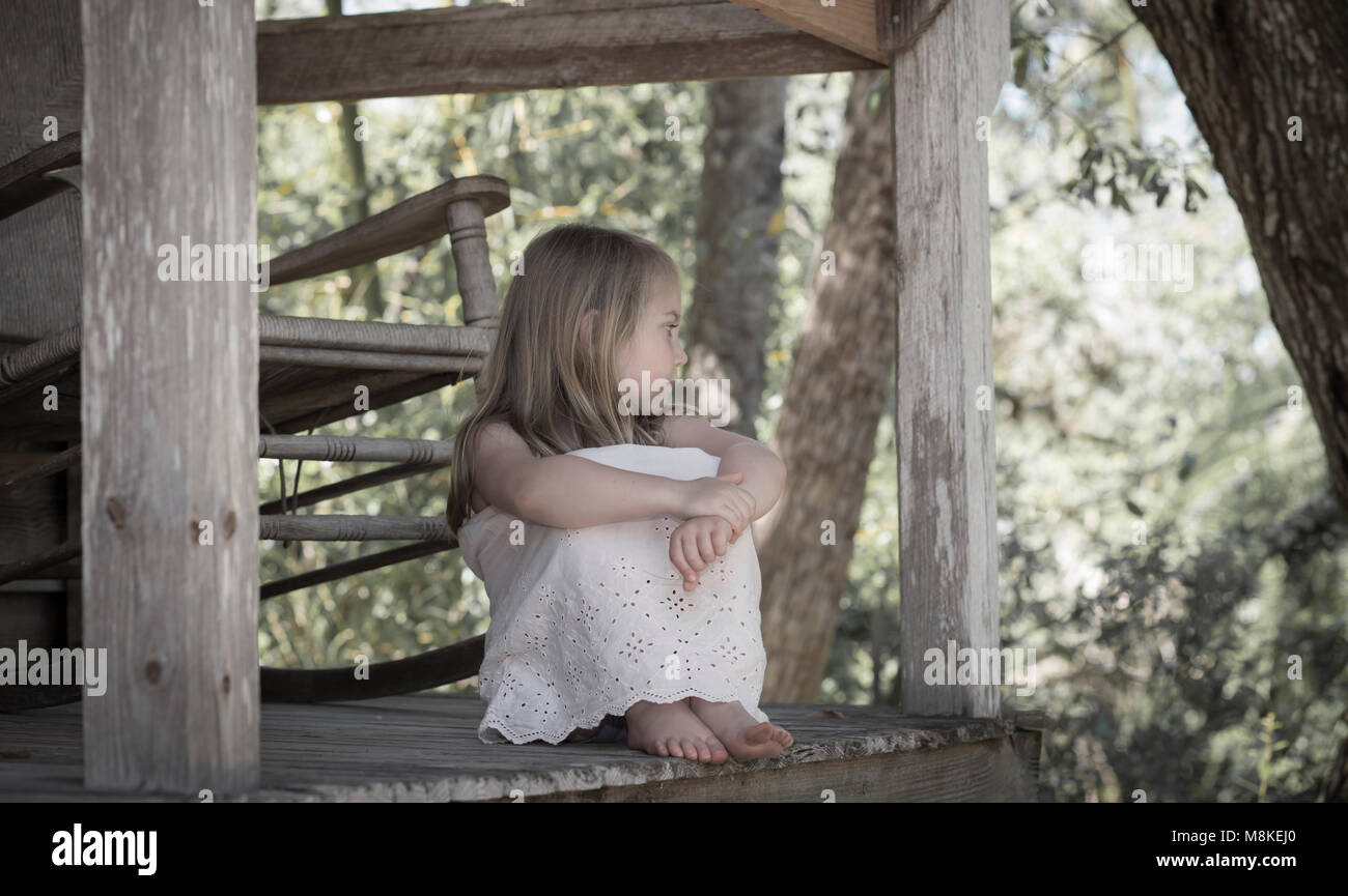 Little girl sitting on a porch barefoot Stock Photo