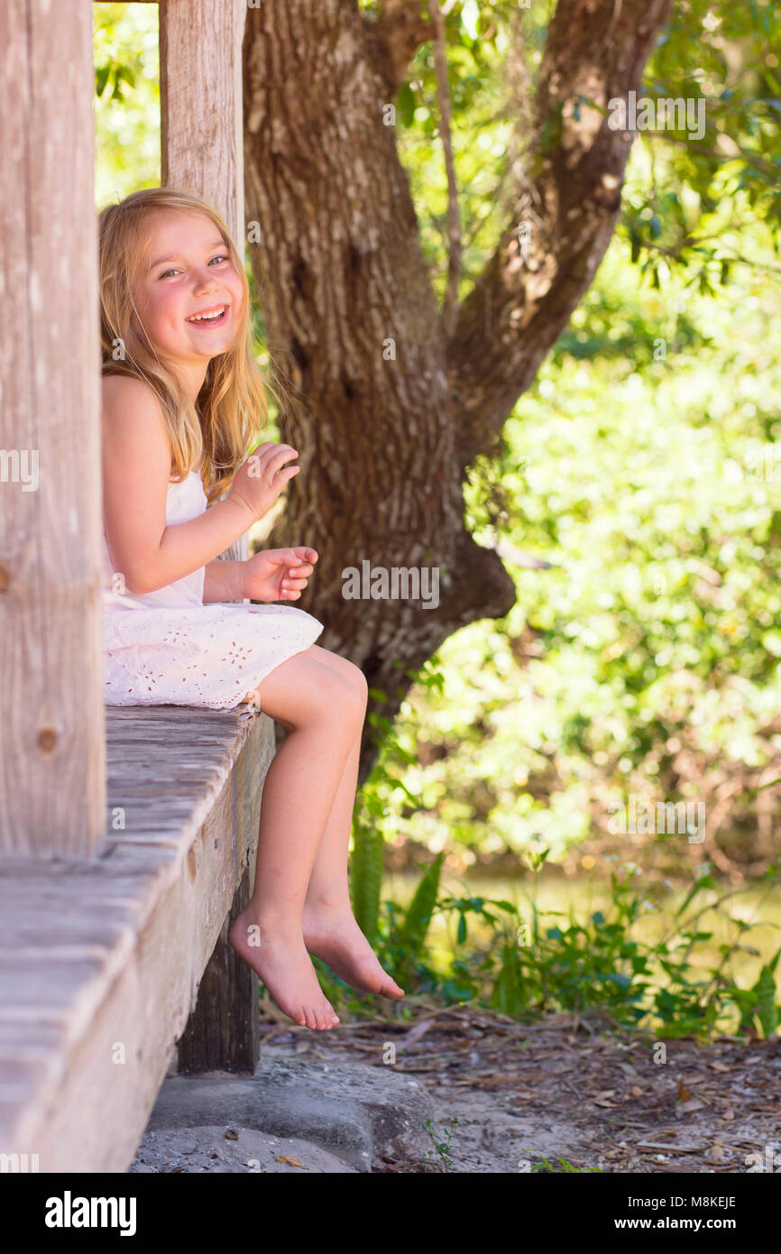 Little girl sitting on a porch barefoot Stock Photo