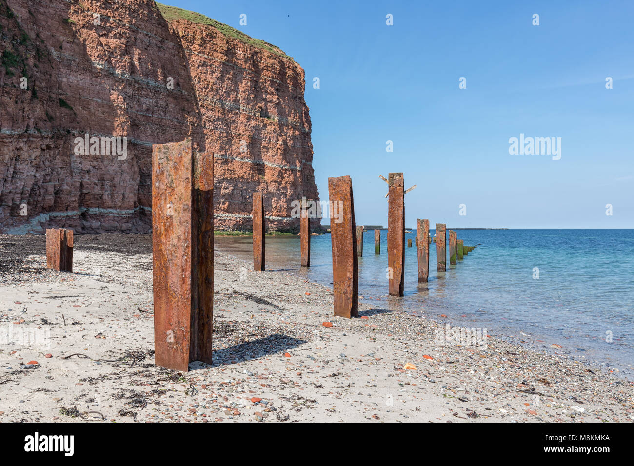 Beach Helgoland island with red cliffs and rusty iron pillars Stock Photo