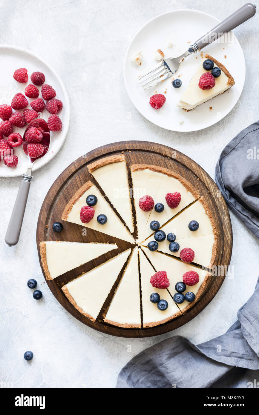 Classic New York cheesecake with fresh raspberries and blueberries on white concrete background, top view Stock Photo
