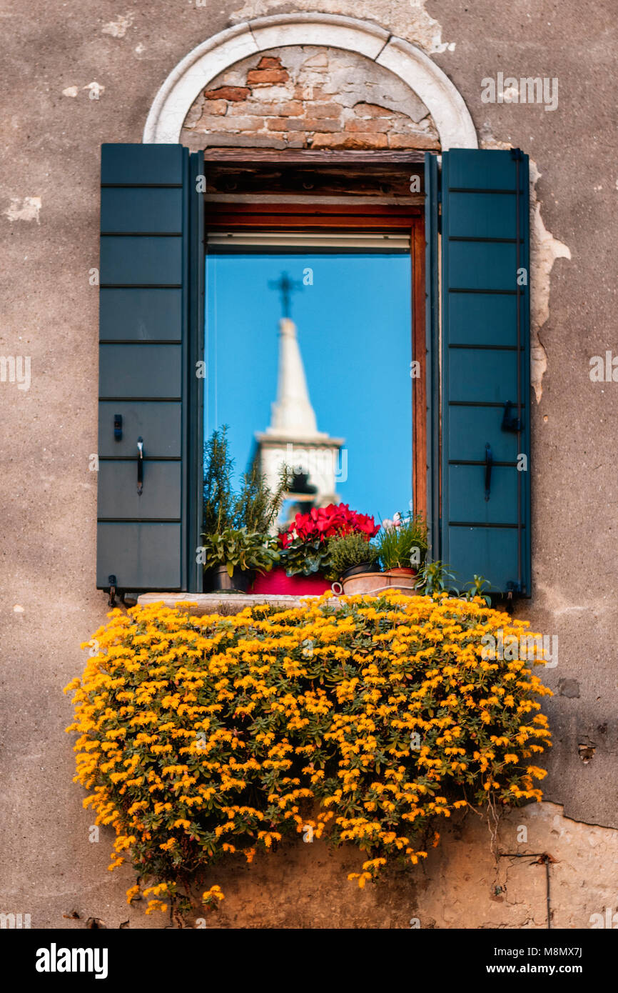 Window reflection of white church with blue sky and flowers in Venice Stock Photo