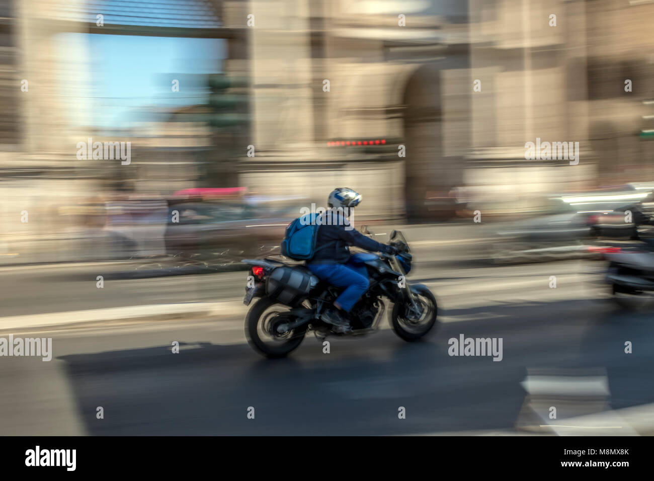Motion blur photograph of helmeted rider on speeding motorbike on main highway in Rome with arches Stock Photo