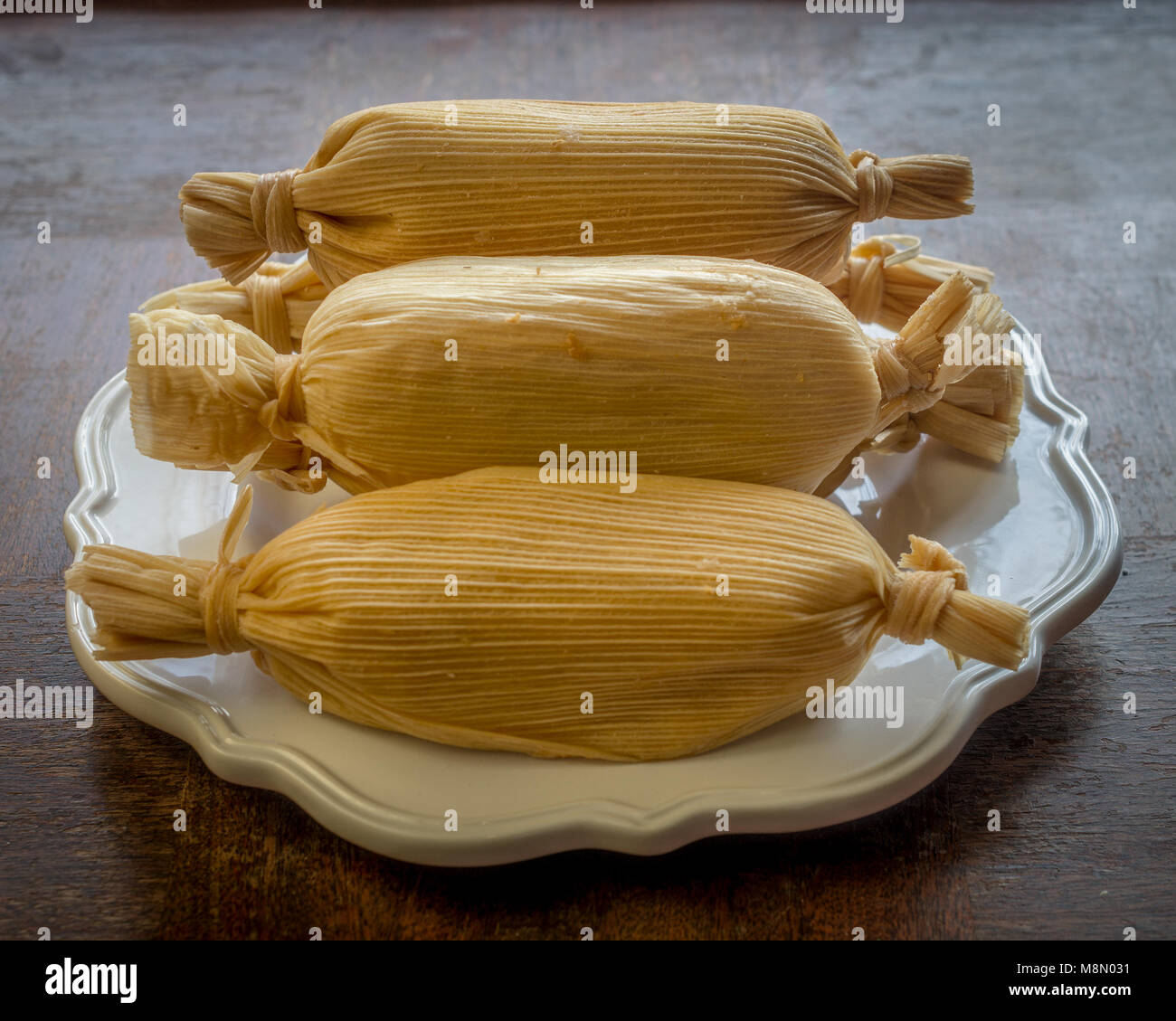 Unwrapped stacked Mexican tamales in white plate on grunge wooden table