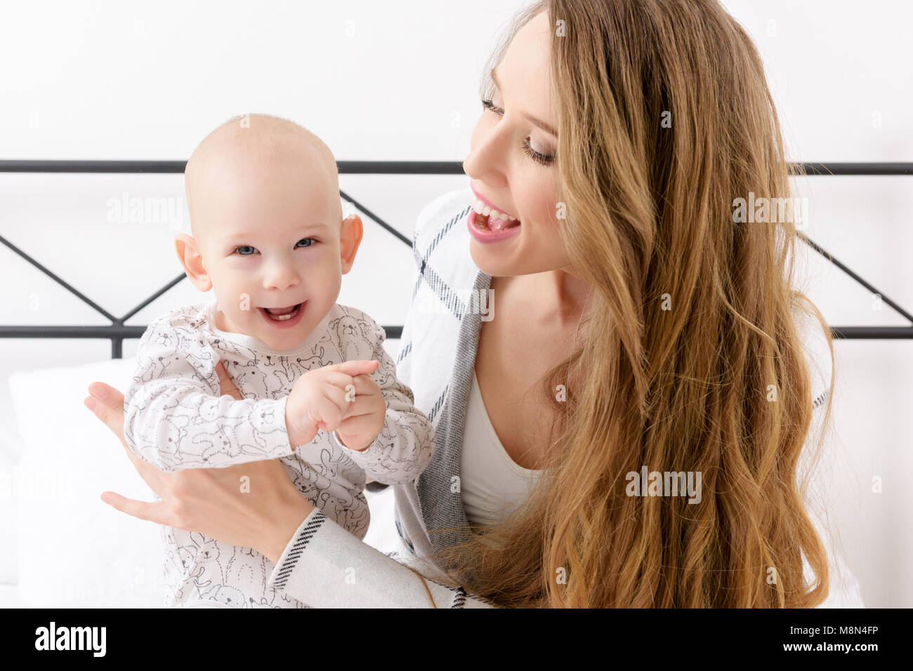 Happy mother and her baby son playing on a bed together. Happy family. Mother and newborn child portrait. Stock Photo