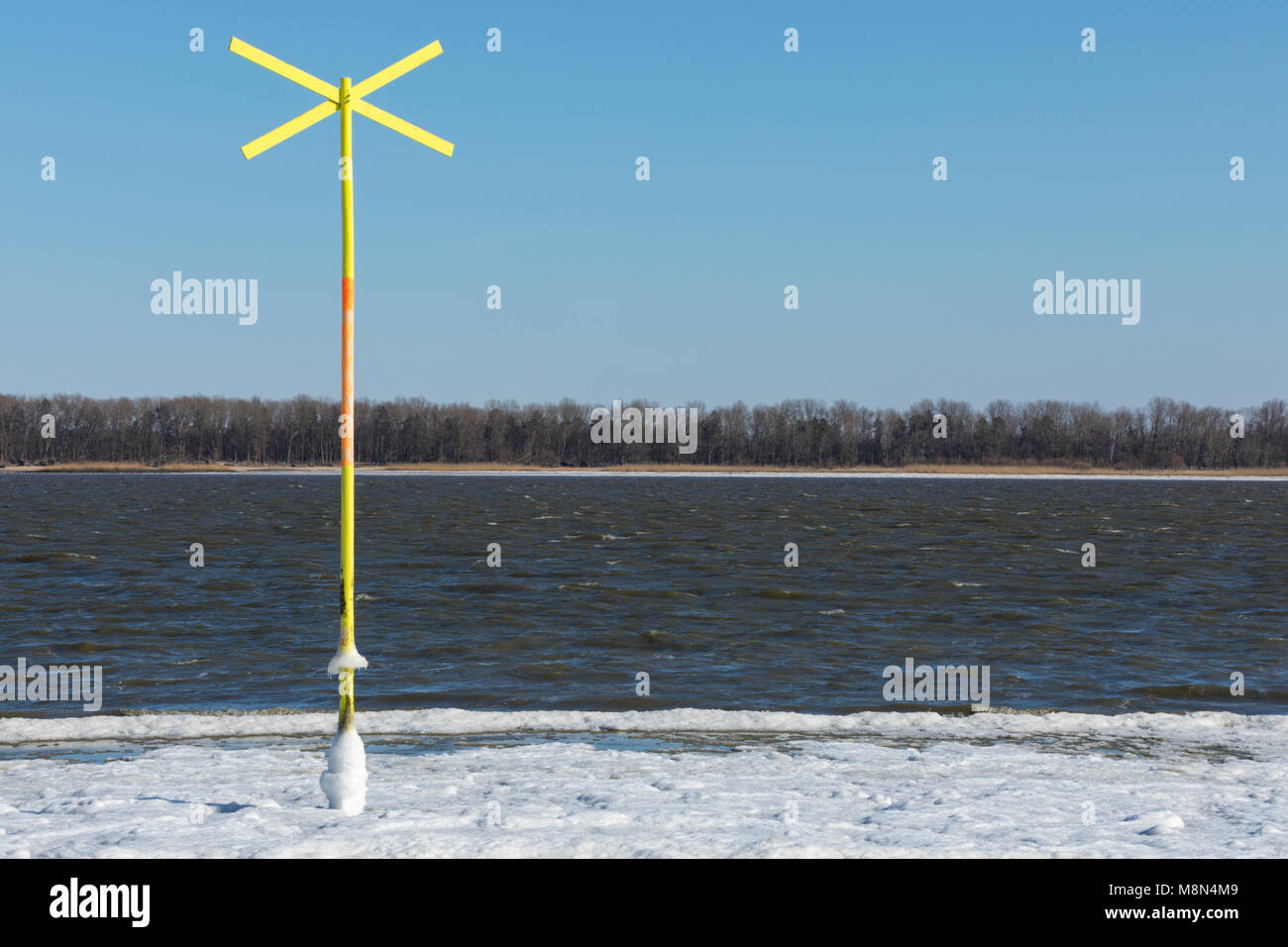 Vibrant yellow shallow water warning sign in partially frozen Elbe river Stock Photo