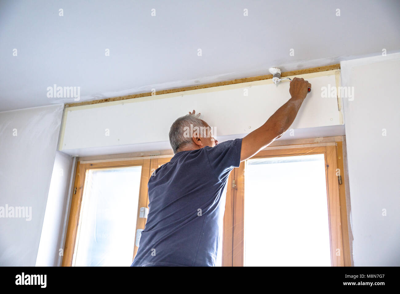 Whitewasher Man At Work Painting A Blank Ceiling With Paint Brush