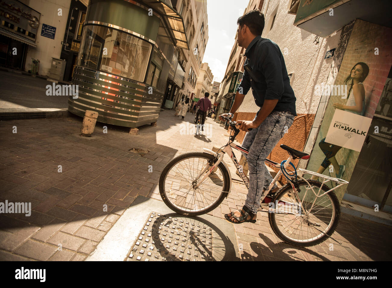 A man on a bicycle riding down the street in Dubai, UAE Stock Photo