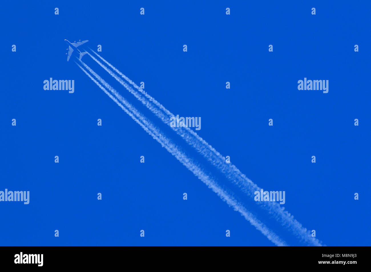 Flying aeroplane with leaving white trails on a blue sky Stock Photo