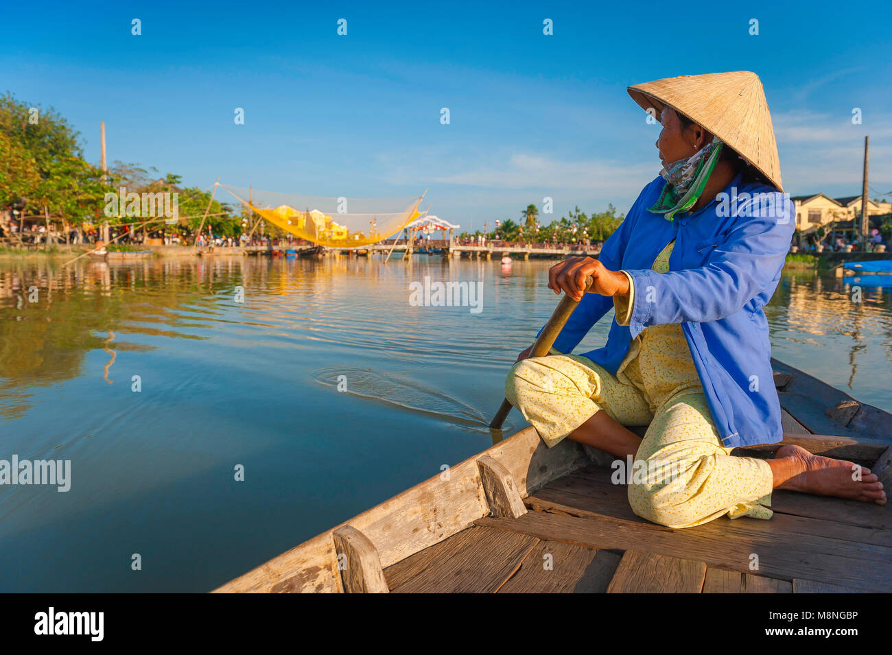 Hoi An river, view of a Vietnamese 'boat-lady' in a conical hat rowing along the Thu Bon River and looking towards the town of Hoi An, Vietnam. Stock Photo