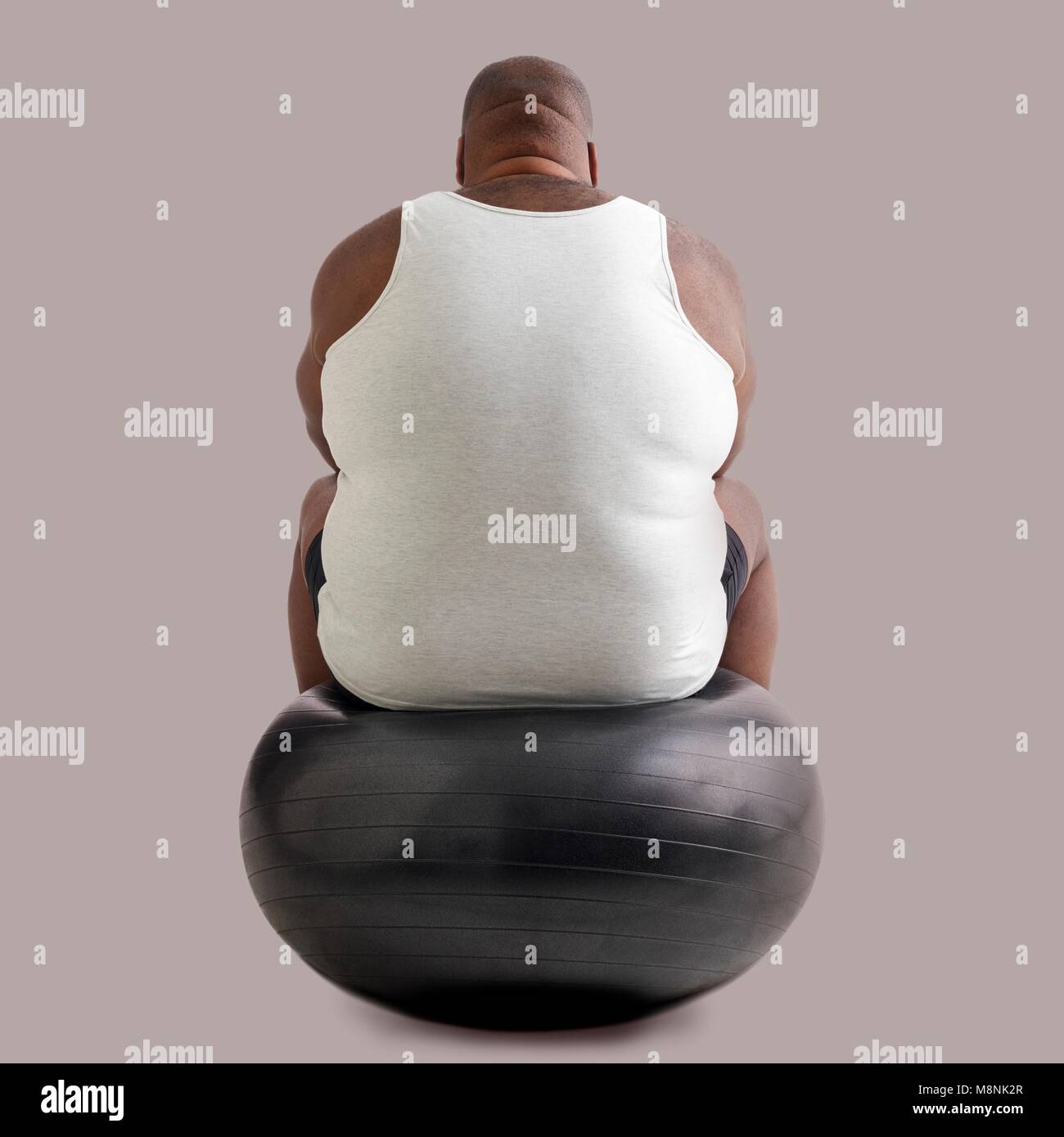 Overweight man sitting on an exercise ball, rear view. Stock Photo