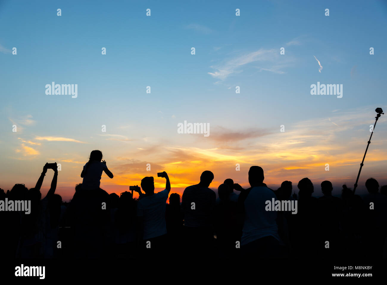 Crowd of people taking pictures of the sunset with mobile phones and selfie stick on a summer night in Florence, Italy Stock Photo
