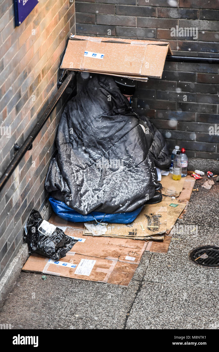 Homeless man huddled in corner of underpass with snow on bedding