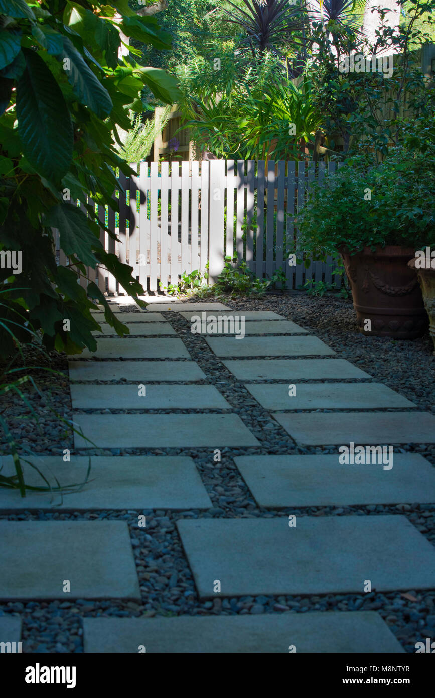 A concrete stepping stone and gravel path leading to a painted picket fence in a North Shore garden of Sydney, Australia Stock Photo