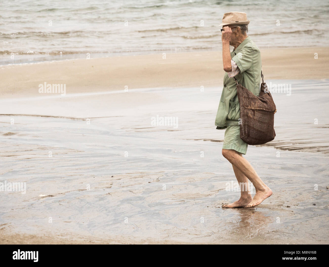 Elderly man walking barefoot on beach Stock Photo