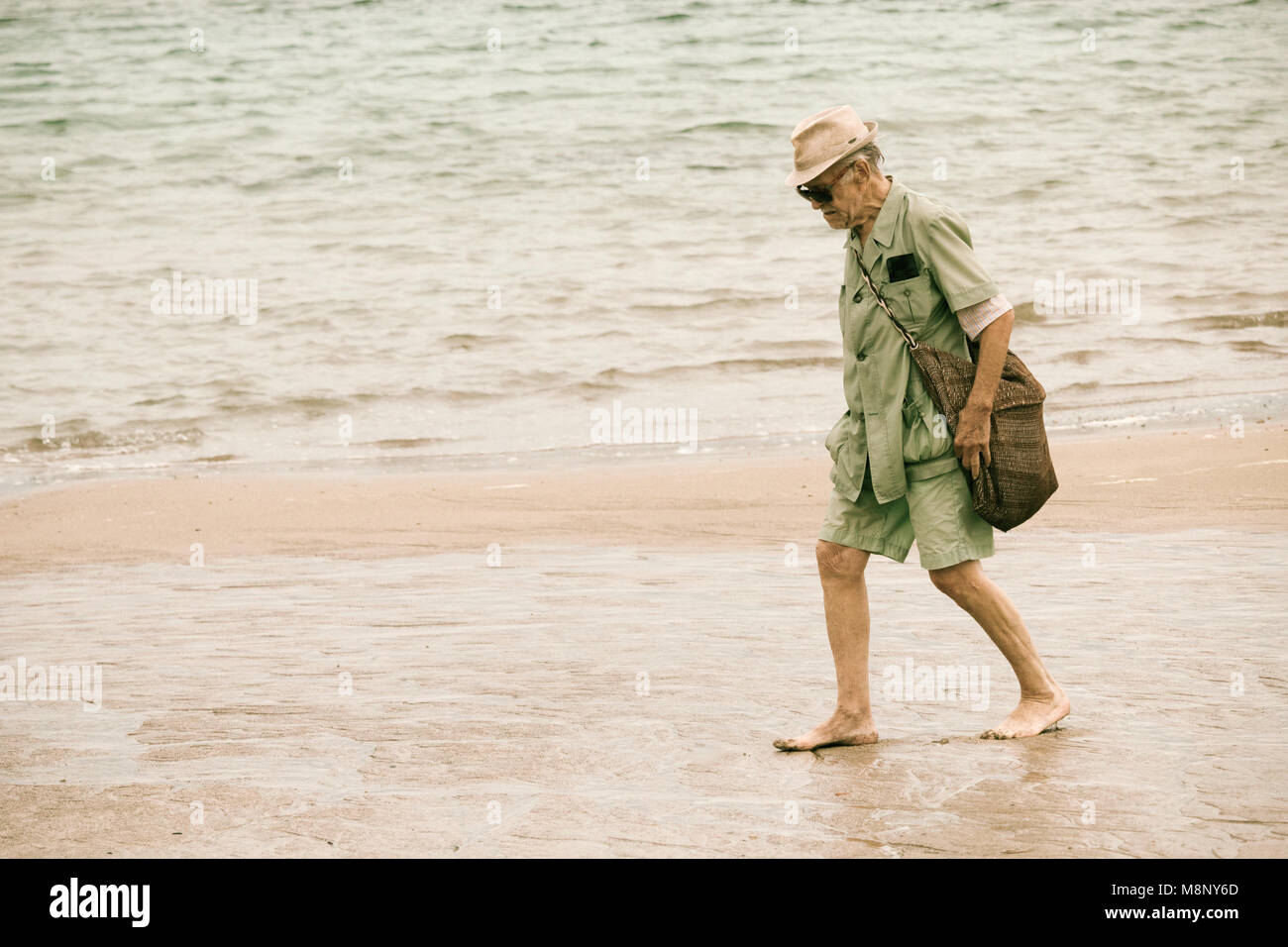 Elderly man walking barefoot on beach Stock Photo