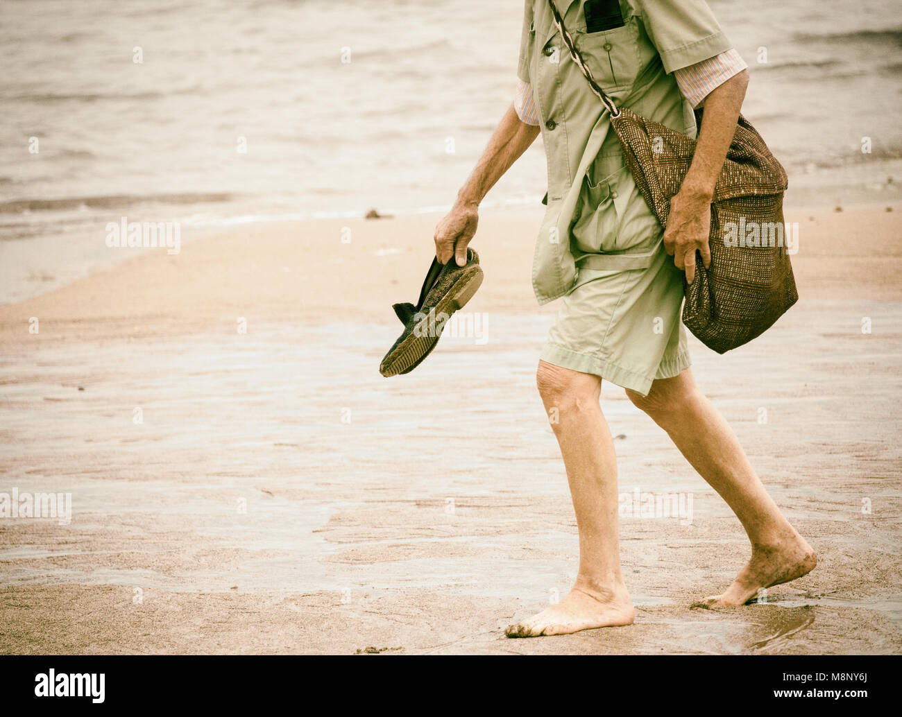 Elderly man walking barefoot on beach Stock Photo