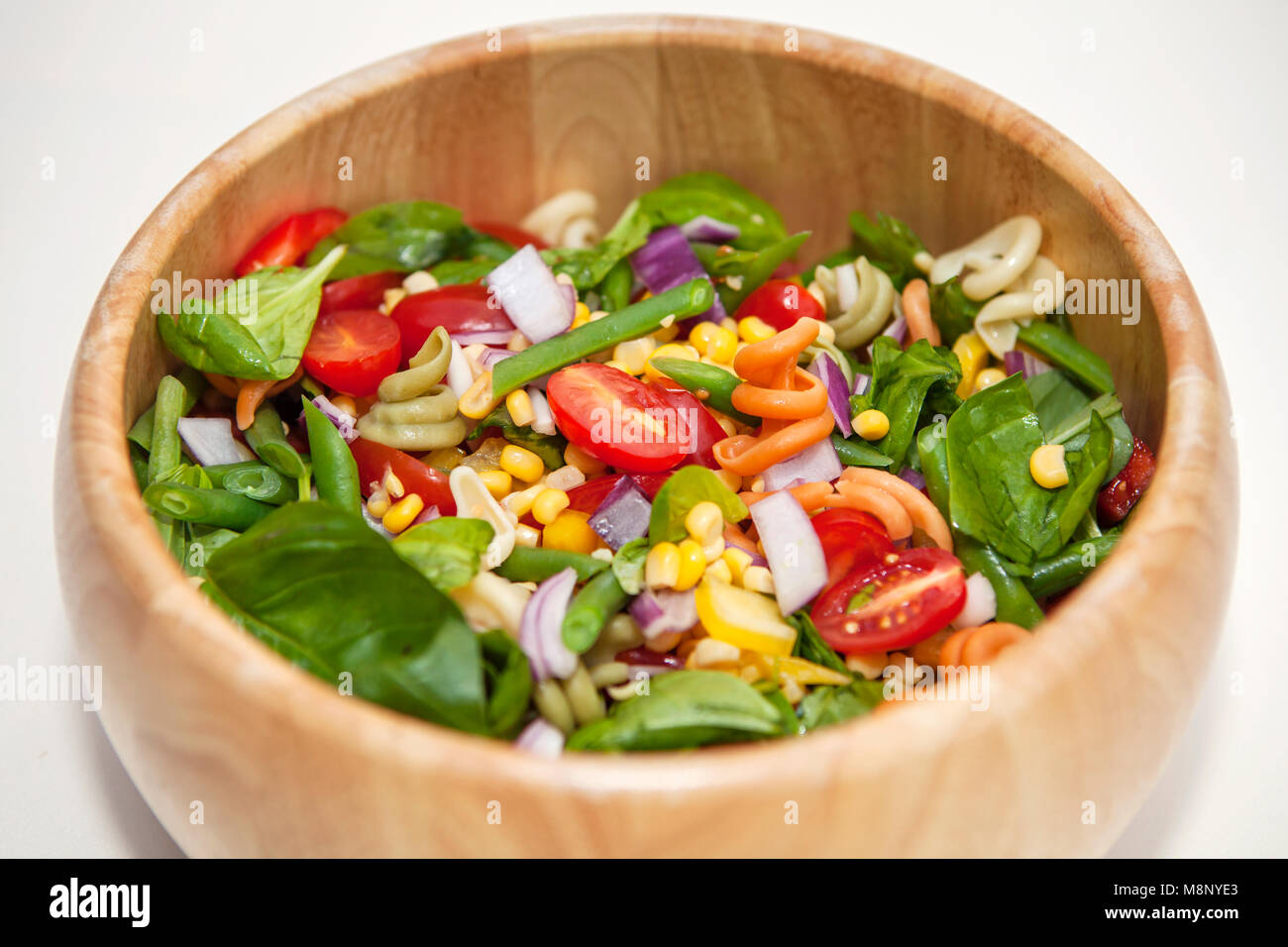 Pasta salad in a wooden bowl, with tomatoes, sweetcorn, onion, spinach Stock Photo