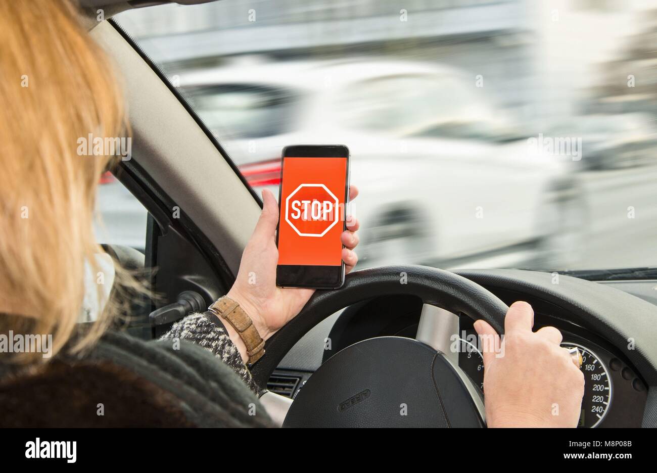 Woman holds a smartphone with stop sign in her hand while driving | usage worldwide Stock Photo