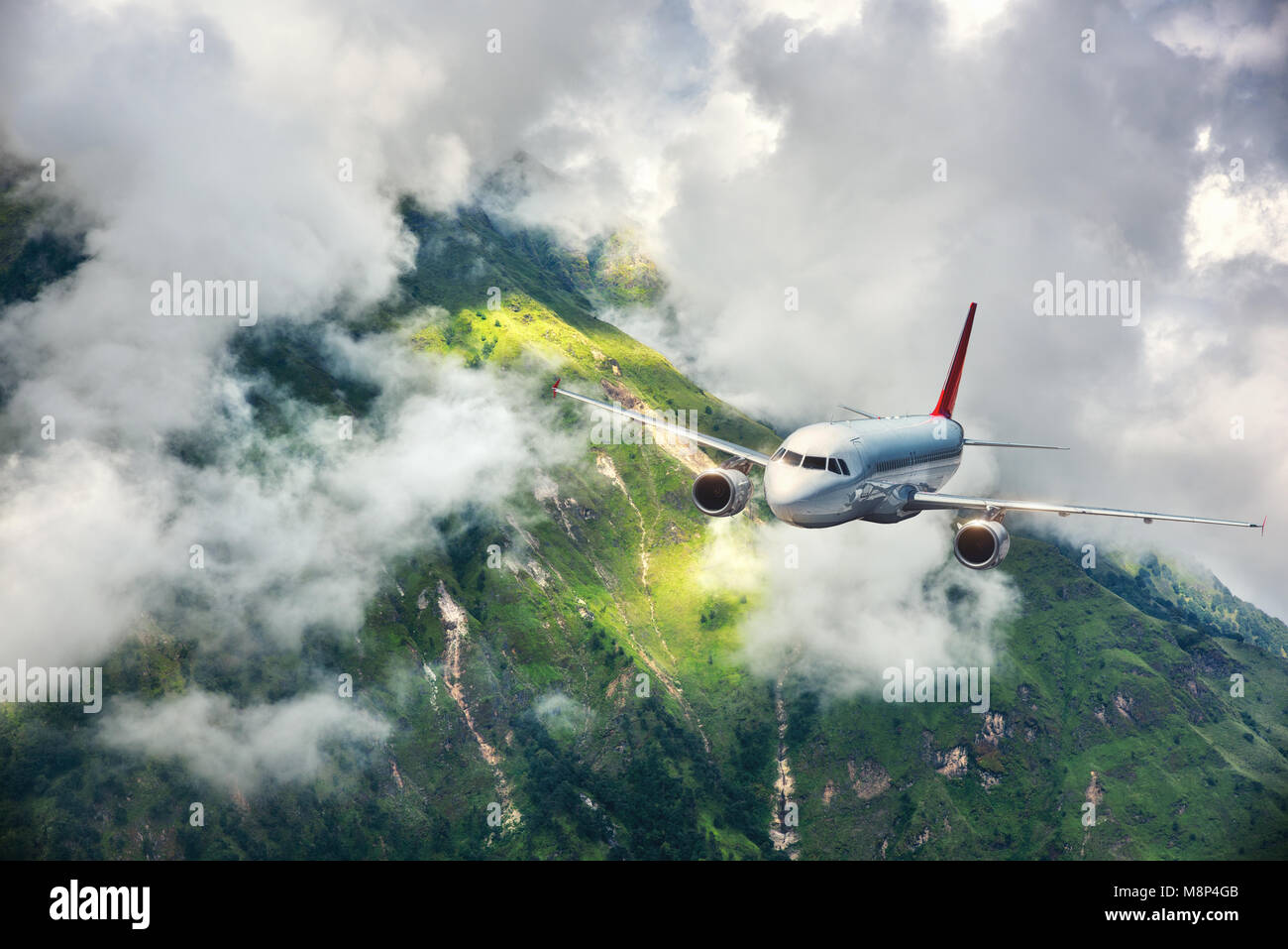 Aerial view of aircraft. Airplane is flying in clouds over mountains with forest at sunset. Landscape with passenger airplane, cloudy sky, trees. Pass Stock Photo