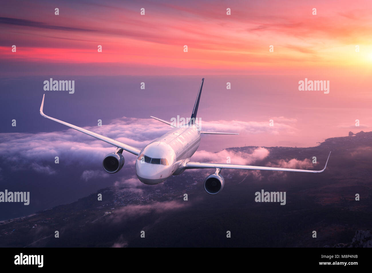 Passenger airplane. Landscape with big white airplane is flying in the red sky over the clouds and sea at colorful sunset. Passenger aircraft is landi Stock Photo