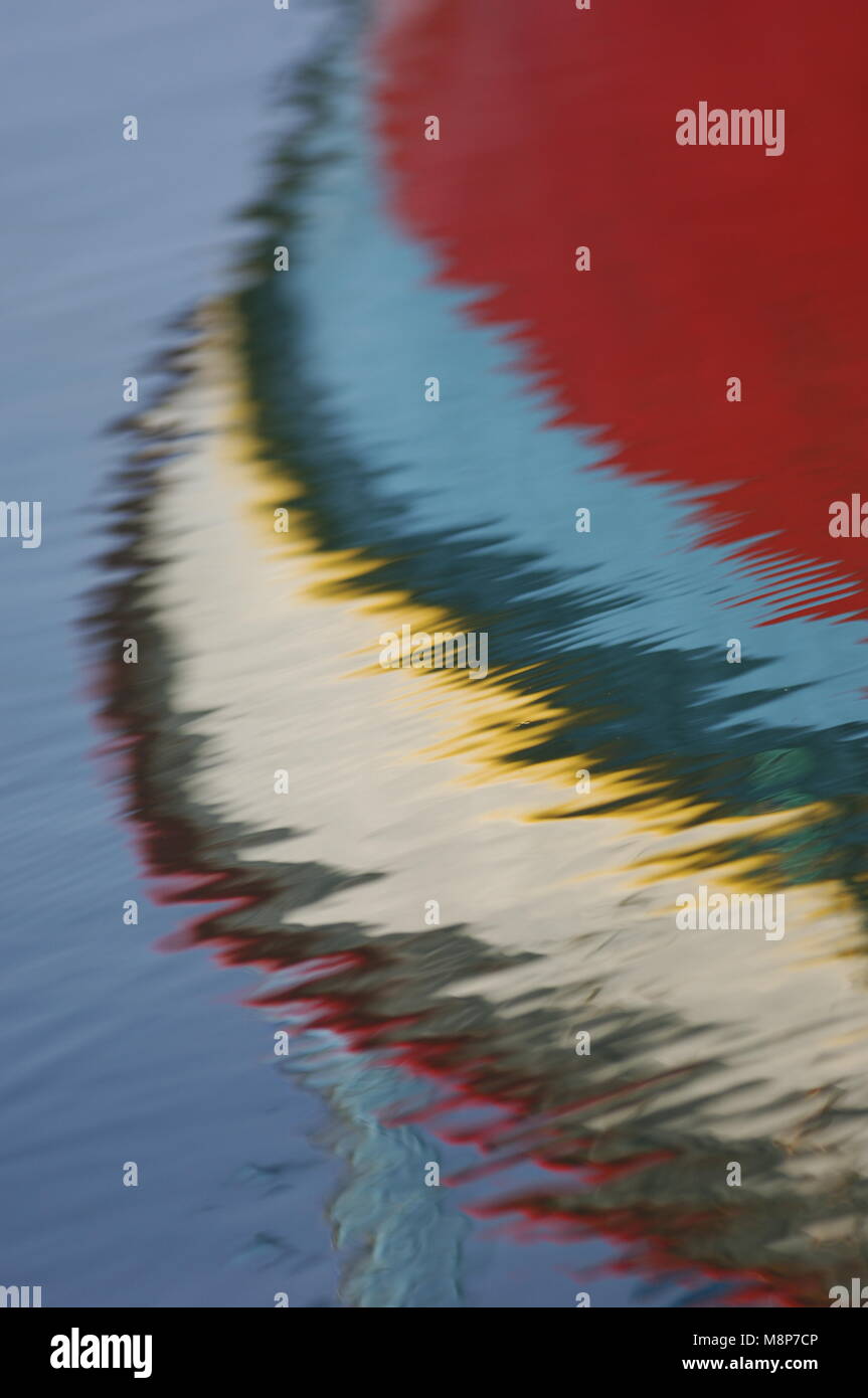 Red blue yellow & white reflections of the hull of a boat in clear blue