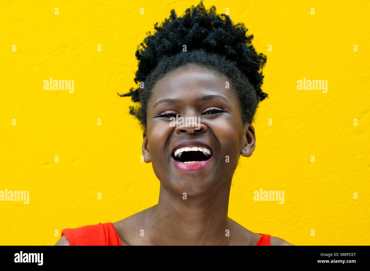 Portrait of a beautiful black colombian model laughing on a yellow monochrome background Stock Photo