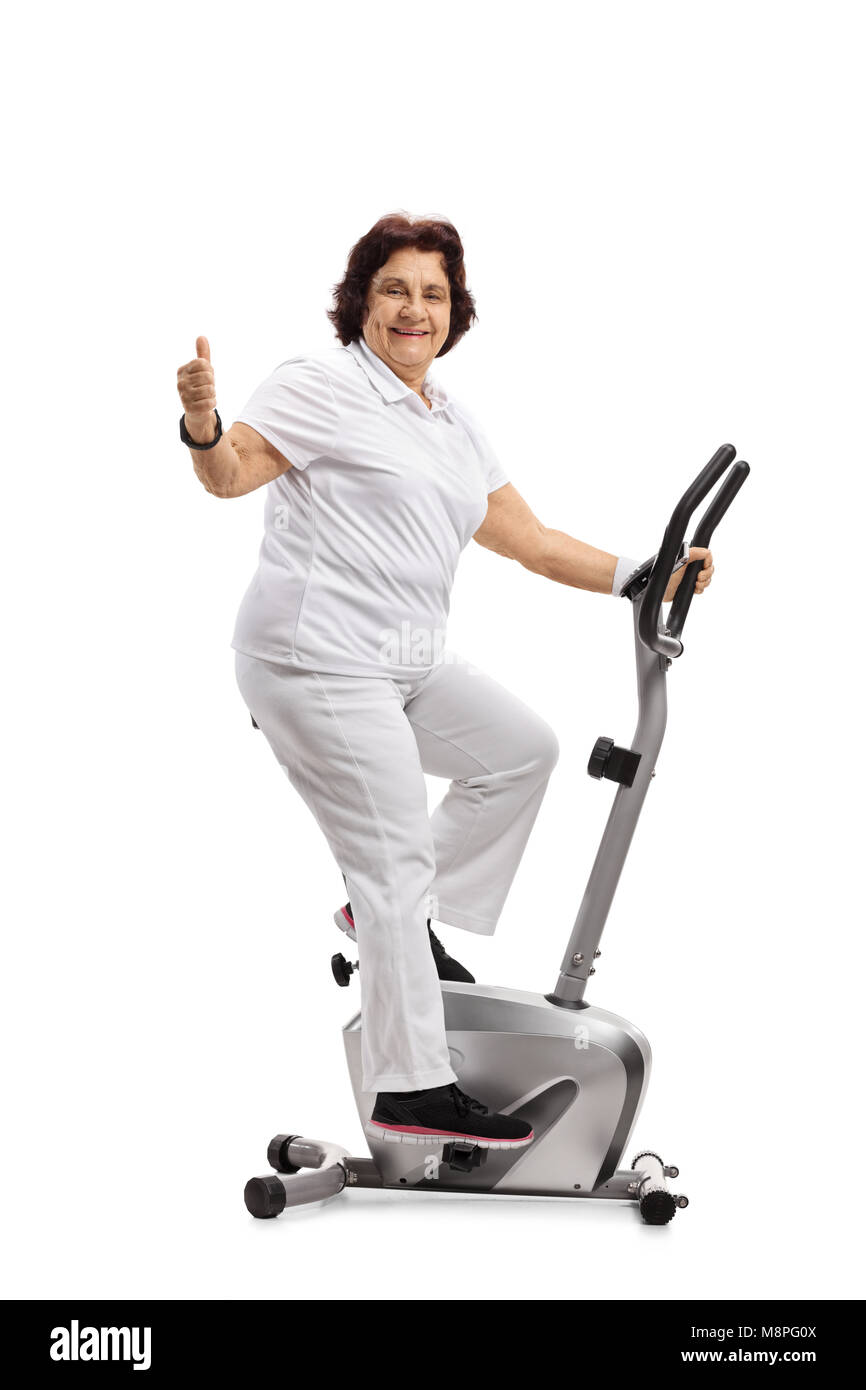 Elderly woman on an exercise bike making a thumb up gesture isolated on white background Stock Photo
