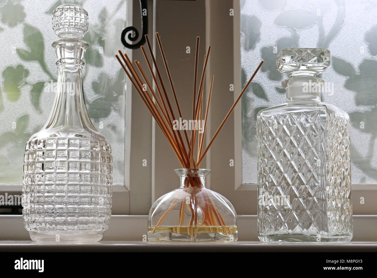 A Reed Diffuser on a windowsill between two decanters Stock Photo