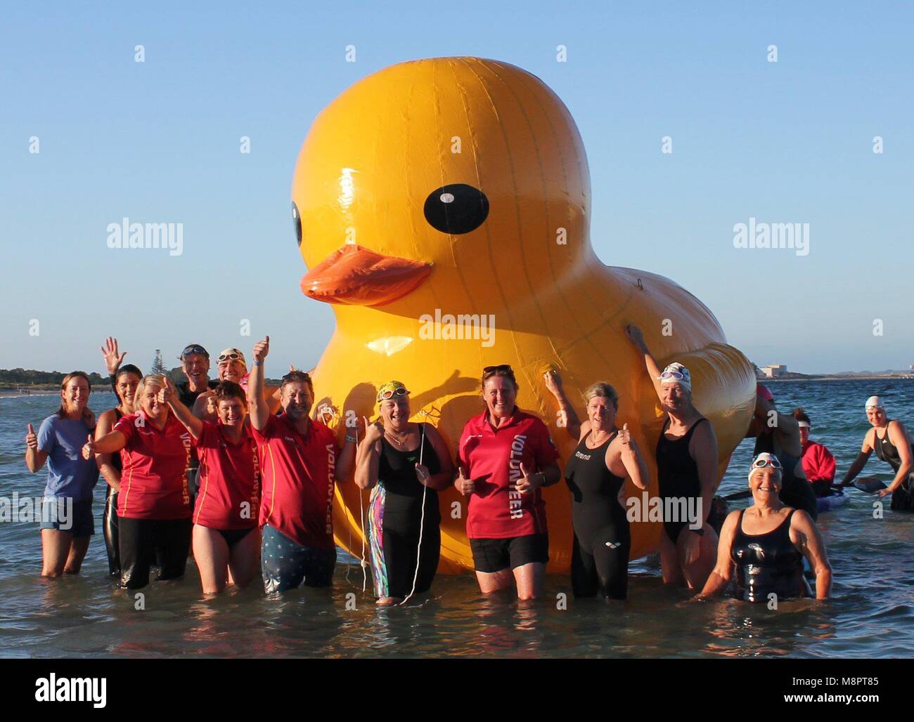 HANDOUT - 27 February 2018, Australia, Coogee Beach: Members are gathered around the duck Daphne, the mascot of the Australian Cockburn Masters Swimming Club. After a week on the high seas the giant yellow squeaking duck reappeared before Australia. The inflatable animal was discovered by a fisherman more than 30 kilometres before the West ccoast as it became known on 19 March 2018. Photo: Nick Wyatt/Cockburn Masters Swimming Club /dpa - ATTENTION: editorial use only in connection with the latest coverage about (the transmission/the film/the auction/the exhibition/the book) and only i Stock Photo