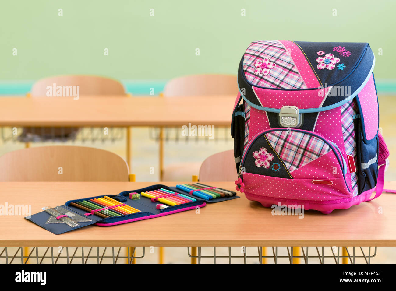 Pink girly school bag and pencil case on a desk in an empty classroom. First day of school concept. Stock Photo